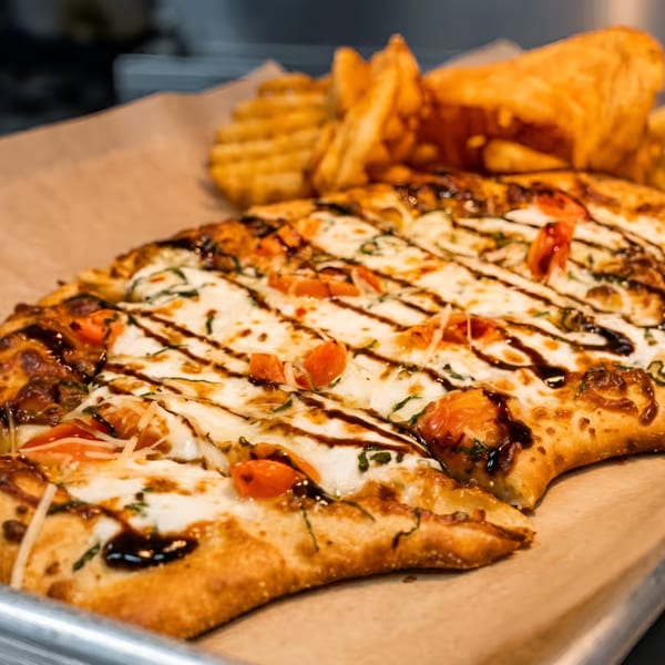 Flatbread pizza with mozzarella, tomatoes, basil, balsamic glaze, and waffle fries on a tray.