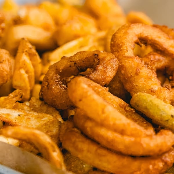 Close-up of golden-brown onion rings and seasoned potato wedges, a delicious fried appetizer.
