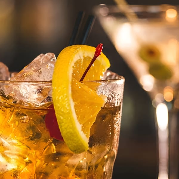 Close-up of an Old Fashioned cocktail with orange slice and cherry, with a martini in the background.