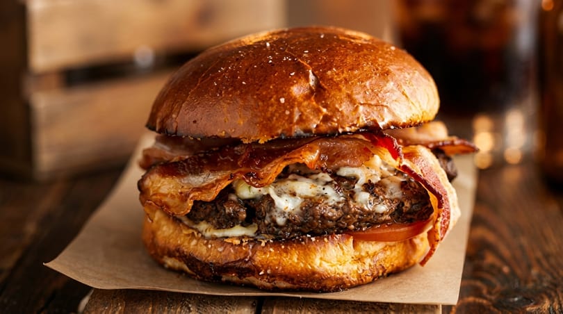 Close-up of a juicy bacon cheeseburger with melted cheese and a toasted bun on a wooden table.